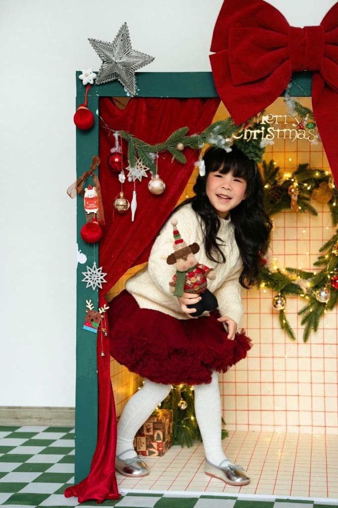 Ảnh gia đình Noel ở Hưng Yên: từ album tham khảo đến buổi hẹn của nhà mình 1 Bé ngồi trên ghế đỏ trước khung vòm Giáng sinh