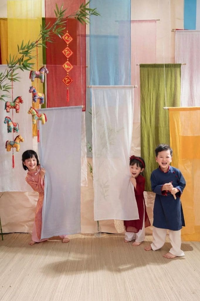 Bé áo dài hồng giơ tay, hai bạn ngồi bên cạnh