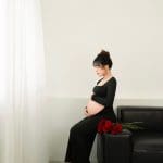 Mẹ bầu mặc váy đen ngồi trên sofa trước cửa sổ sáng