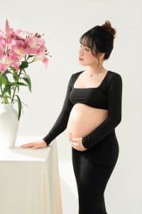 Trang phục chụp bầu: váy, áo dài hay đồ thường, mặc sao cho thoải mái? 5 Mẹ bầu đứng cạnh cửa sổ và hoa hồng, một tay đặt lên khung cửa
