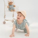 Bé bò trên nền sáng cạnh gấu bông và đạo cụ ghế
