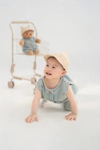 Bé bò trên nền sáng cạnh gấu bông và đạo cụ ghế