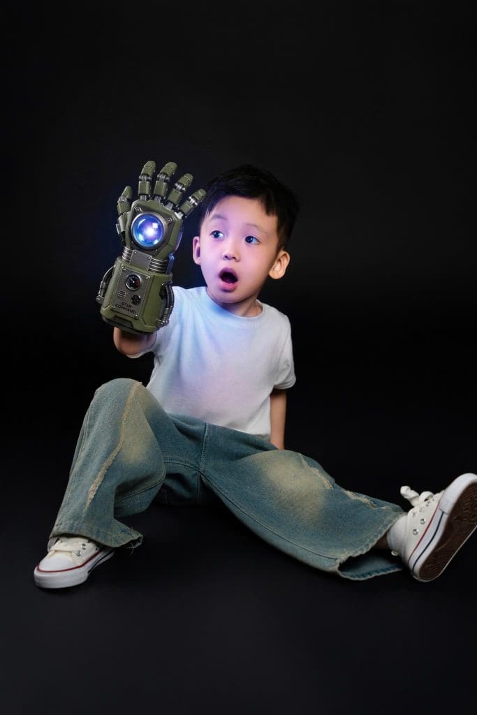Bé mặc áo xám ngồi cầm đồ chơi trên nền tối