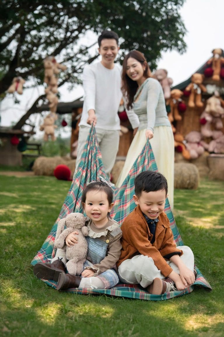 Ba mẹ đứng phía sau hai con ngồi trên bãi cỏ