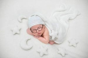 Bé sơ sinh đội mũ và đeo kính tròn ngủ trên nền trắng