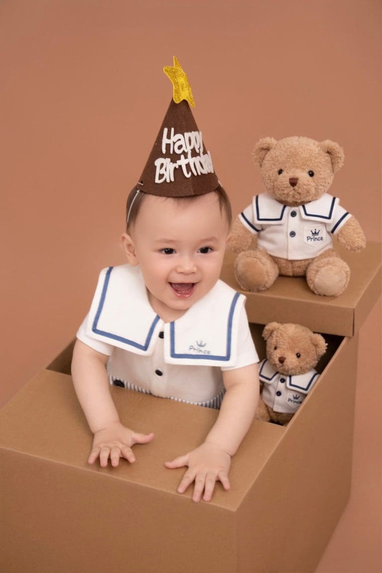 Bé vịn mép hộp giấy, bên cạnh là gấu bông màu nâu