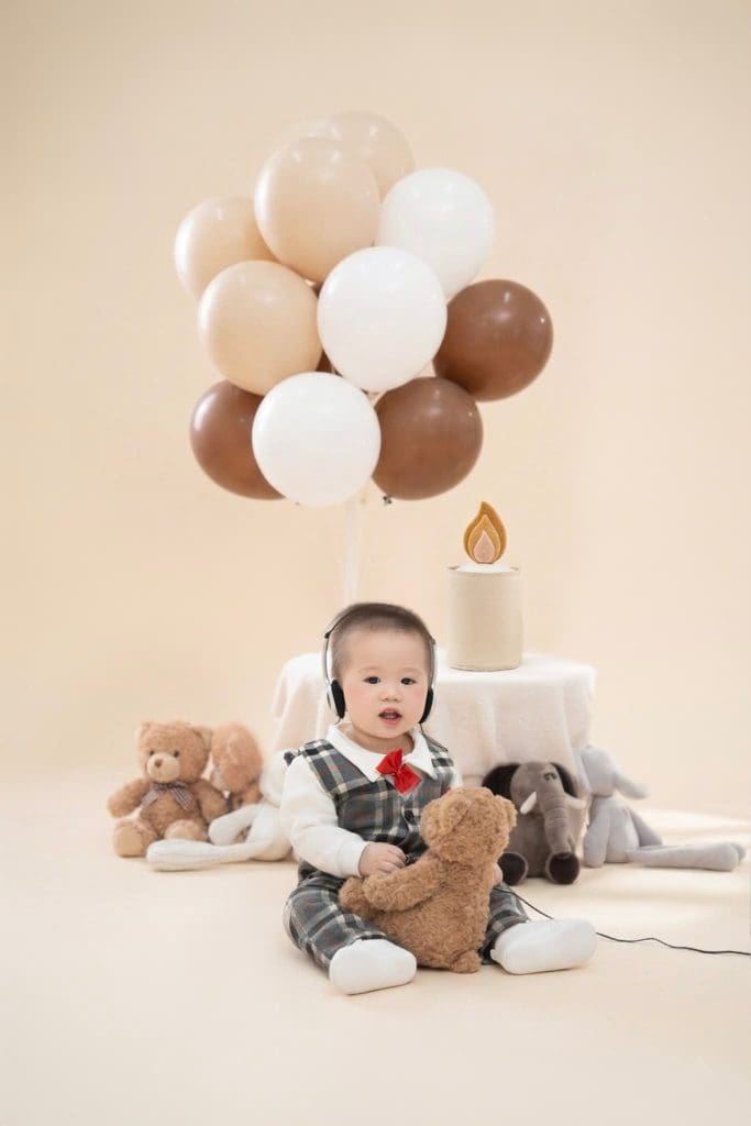 10 ý tưởng chụp ảnh sinh nhật cho bé 1 tuổi dễ điều chỉnh 1 Bé mặc áo kẻ ngồi cạnh bánh sinh nhật trên nền màu be