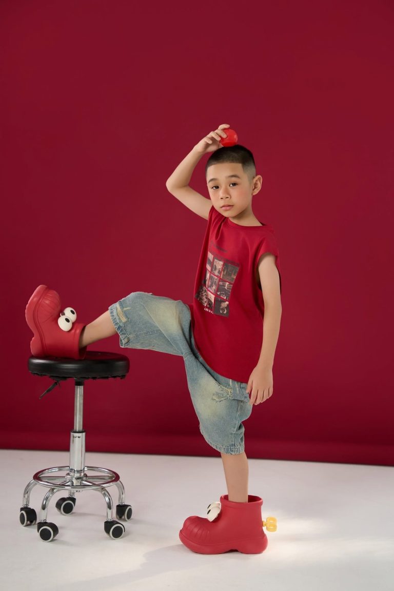 Mẫu nhí tạo dáng toàn thân với áo đỏ trước nền đỏ